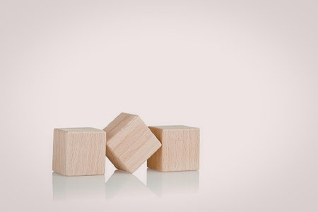 Three wooden blocks are arranged on a white surface. Two blocks are cylindrical and one is cuboid.