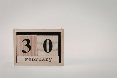 A wooden perpetual calendar block displaying the date February 30, set against a plain white...