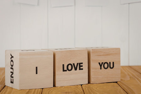 Three wooden blocks with the words 'ENJOY', 'I', 'LOVE', 'YOU' on them, arranged on a wooden...