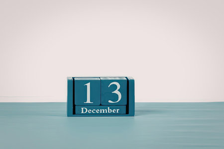 A small blue block calendar displaying the date 13 December on a light blue surface with a white...