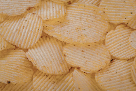 A close-up view of a pile of crispy, golden-brown potato chips with ridged texture.