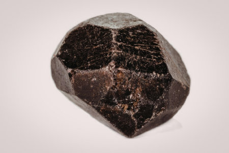 A large dark brown crystal gemstone with a rough surface and multiple facets, set against a plain...