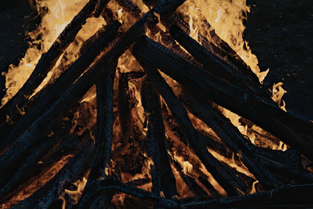 A large fire is burning in the night, with flames reaching up into the darkness. The fire is made up...