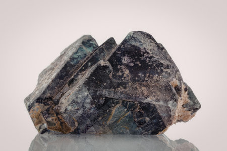 A large, dark purple rock with flecks of green and brown sits on a reflective surface. The rock has...