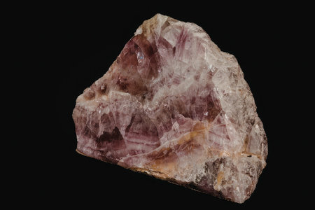 A raw, unpolished pink quartz crystal with a rough texture and a deep pink color, set against a black background.の写真素材