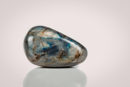 A polished labradorite stone with flashes of blue and gold, set against a white background.