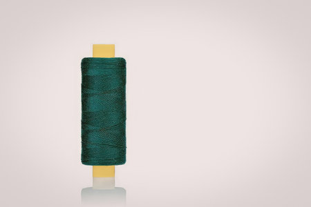 A spool of green thread on a yellow and white spool against a white background.
