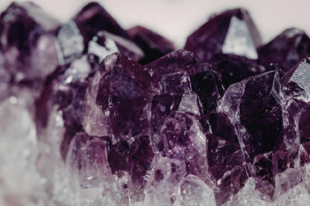 A close-up view of a cluster of sharp-edged amethyst crystals with a deep purple color and a rough,...