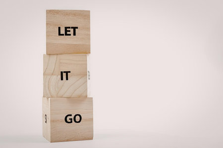 A stack of three wooden blocks with the words 'LET', 'IT', and 'GO' printed on them, against a white...