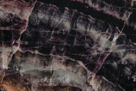A close-up view of a dark purple amethyst stone with visible cracks and veins, showcasing its...