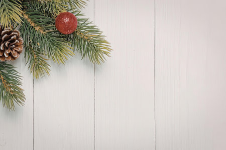 A Christmas tree branch with pine needles, a pine cone, and a red ornament on a white wooden background.の写真素材