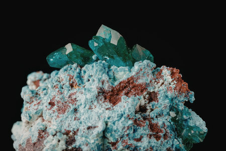 A close-up photograph of a vibrant emerald crystal cluster situated atop a colorful rock formation, set against a stark black background.の写真素材