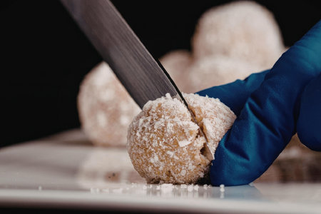 A gloved hand cutting a ball with a knife on a white surface with other balls in the background.