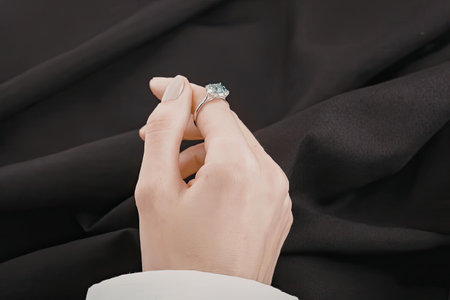 A hand wearing a diamond ring on a black fabric background