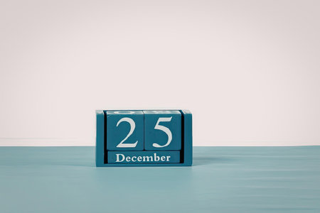 A small blue block calendar displaying the date December 25 on a light blue surface with a white...