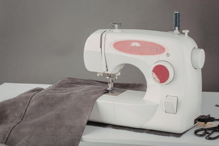 A white and pink sewing machine with a piece of gray fabric under the needle on a white table.