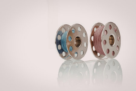 Two spools of thread, one blue and one red, with a reflective surface underneath.の写真素材