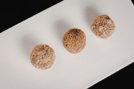 Three round food items, possibly desserts or snacks, coated with brown material, placed on a white...