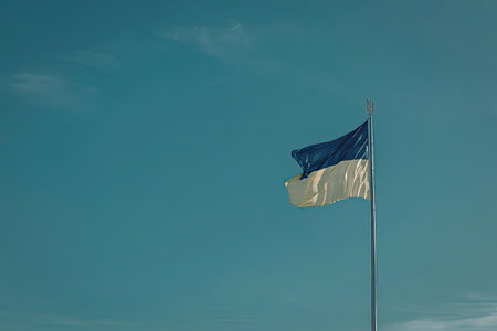 The Ukrainian flag flying on a pole against a clear blue sky.