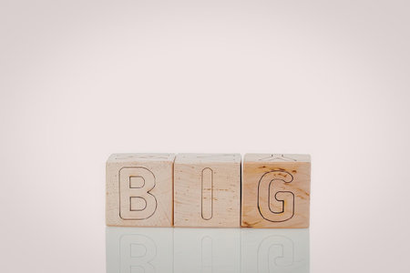 A set of three wooden blocks with the letters B, I, and G carved into them, forming the word 'BIG'. The blocks are light brown in color and have a smooth texture. They are arranged horizontally and have a slight reflection on the surface below.の写真素材