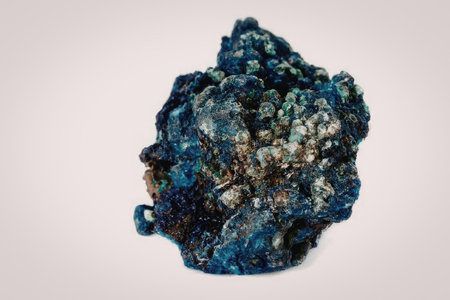 A vibrant blue mineral specimen with golden flecks and a rough, rocky texture, set against a plain...