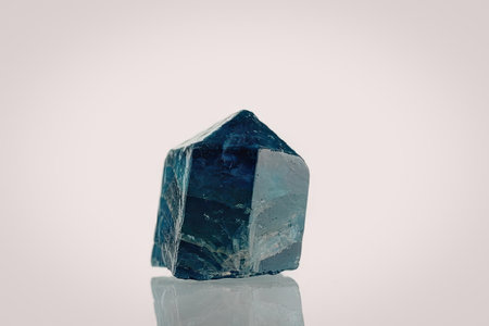 The image shows a single blue crystal with a pointed top and flat base, set against a white...
