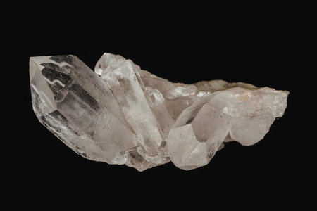 A cluster of clear quartz crystals with a rough, rocky texture and sharp points, set against a solid black background.の写真素材