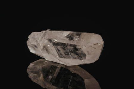A large clear crystal sitting on a reflective black surface with a white background