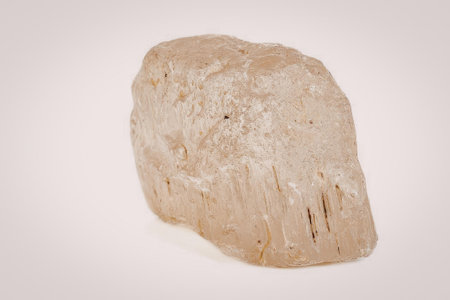 A large, beige-colored rock with a rough texture and irregular shape, set against a plain white...