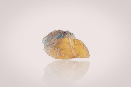 A large yellow gemstone with blue and orange hues sits on a white surface, reflecting its vibrant...