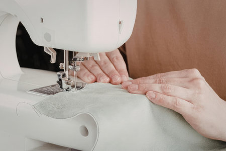 A person is using a white sewing machine to sew a piece of green fabric.