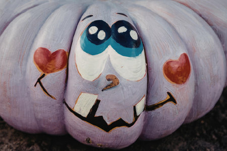 A close-up of a purple pumpkin with a smiling face painted on it, featuring blue eyes, a brown nose, and a wide mouth, and two red hearts on either side of its face.の写真素材