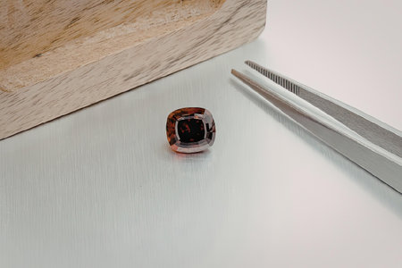 a small red gemstone next to metal tweezers on a white surface with a wooden block