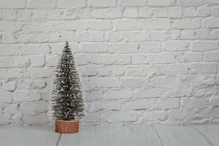 a small pine tree in a brown pot is placed on a gray wooden floor in front of a white painted brick wallの写真素材