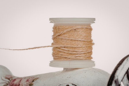A spool of twine is placed on a white surface, with some of the twine unwound to the left. The spool...