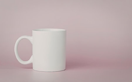 A white mug is placed on a pink surface and background. The mug has a handle on the left side and is empty.の写真素材