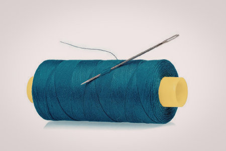 A spool of blue thread with a needle on top, isolated on a white background.