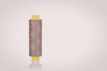 A spool of brown thread on a yellow spool against a white background
