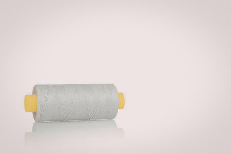 A spool of white thread with yellow plastic ends on a white background