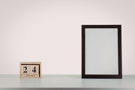 A minimalist still life composition featuring a small wooden calendar with the date 24 and a blank...