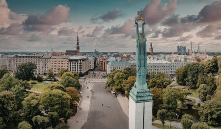 Aerial view of a city with a prominent green statue in the foreground, surrounded by lush trees and buildings in the background under a cloudy sky.の写真素材