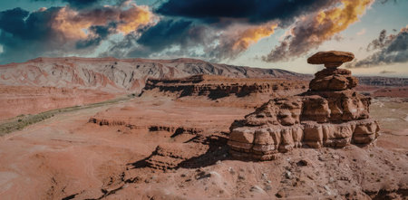 A desert landscape featuring a unique rock formation with a large cap rock on top, set against a backdrop of red sand and a dramatic cloudy sky.の写真素材