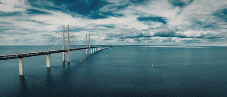 A long bridge stretches over a large body of water under a blue sky with white clouds.