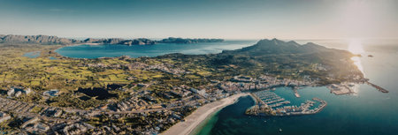 A panoramic aerial view of a coastal town with a marina, surrounded by lush greenery and mountains,...