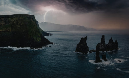 A dramatic coastal landscape featuring rugged rock formations in the ocean, with a large cliff on...