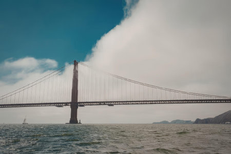 The Golden Gate Bridge stands tall under a partly cloudy sky, with the water below reflecting the...