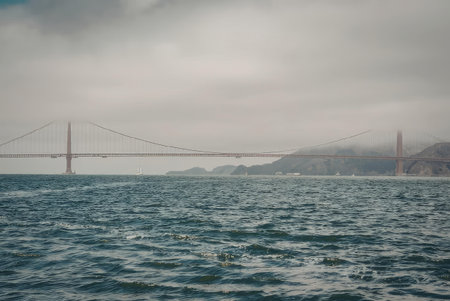 The image shows the Golden Gate Bridge on a cloudy day, with the bridge's iconic towers rising above...