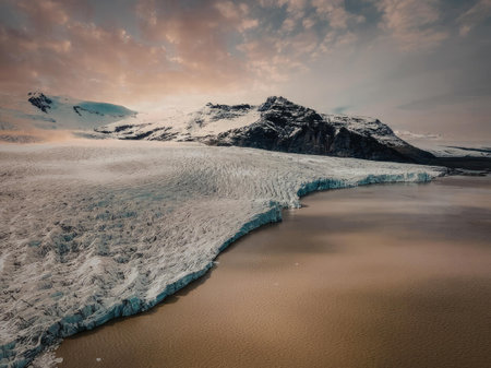 A breathtaking landscape of a glacier meeting the ocean at sunset, with snow-capped mountains in the...