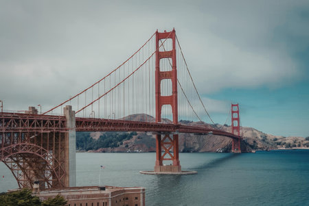 The iconic Golden Gate Bridge stands majestically under a cloudy sky, its distinctive red-orange...