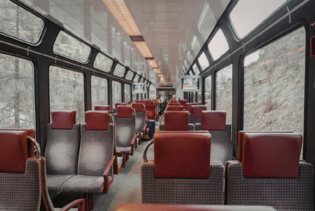 The image shows the interior of a train with rows of red and gray seats facing each other, large...